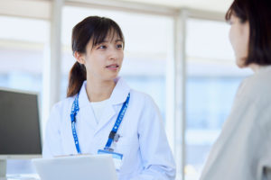 病院の診察室にて女性患者の診察を行う女性医師